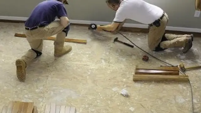Two workers kneeling on a floor measuring and fitting boards during repairs
